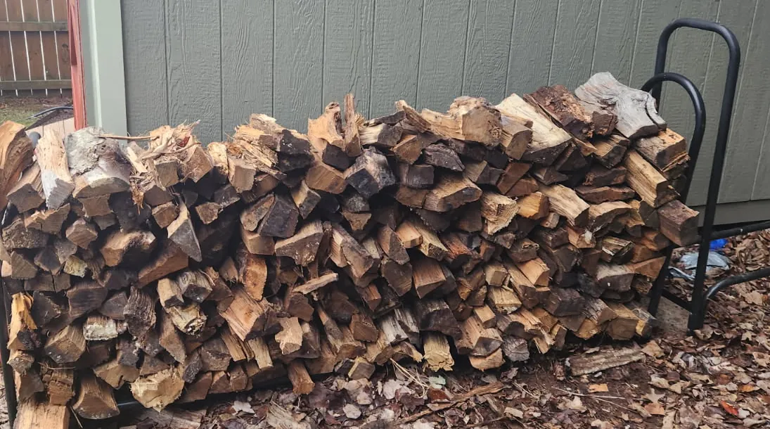 A rack of split hardwood stacked end to end against the side of a shed